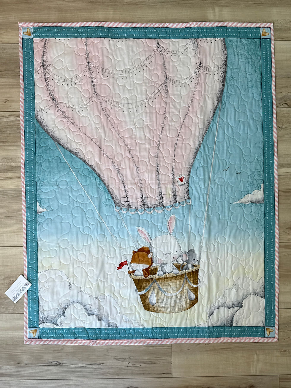 Baby quilt featuring bunny and friends in cream hot air balloon on soft blue sky background with teal borders