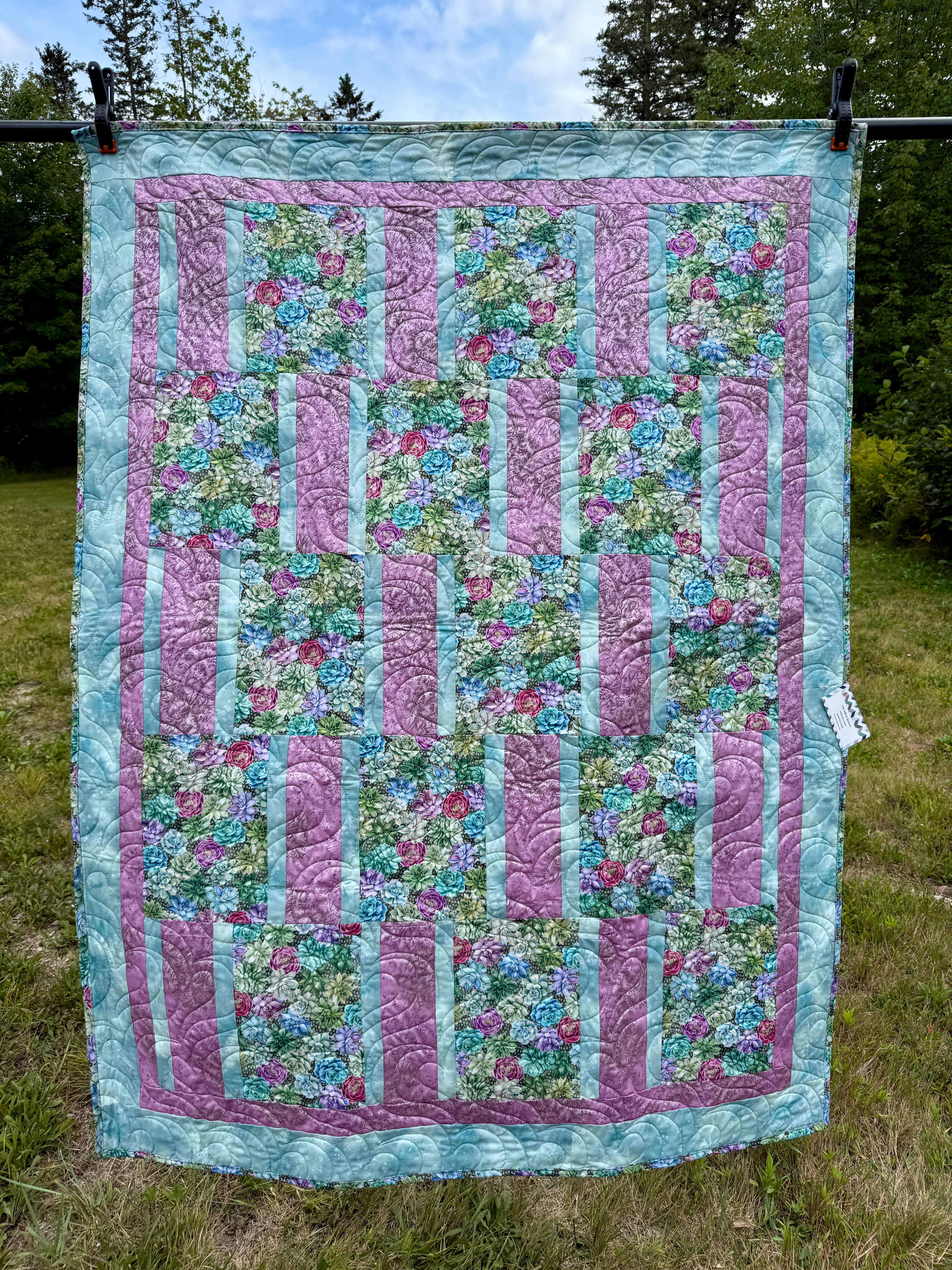 Handmade lap quilt with realistic succulent print blocks in green, teal, pink, and magenta, alternating with pink and teal