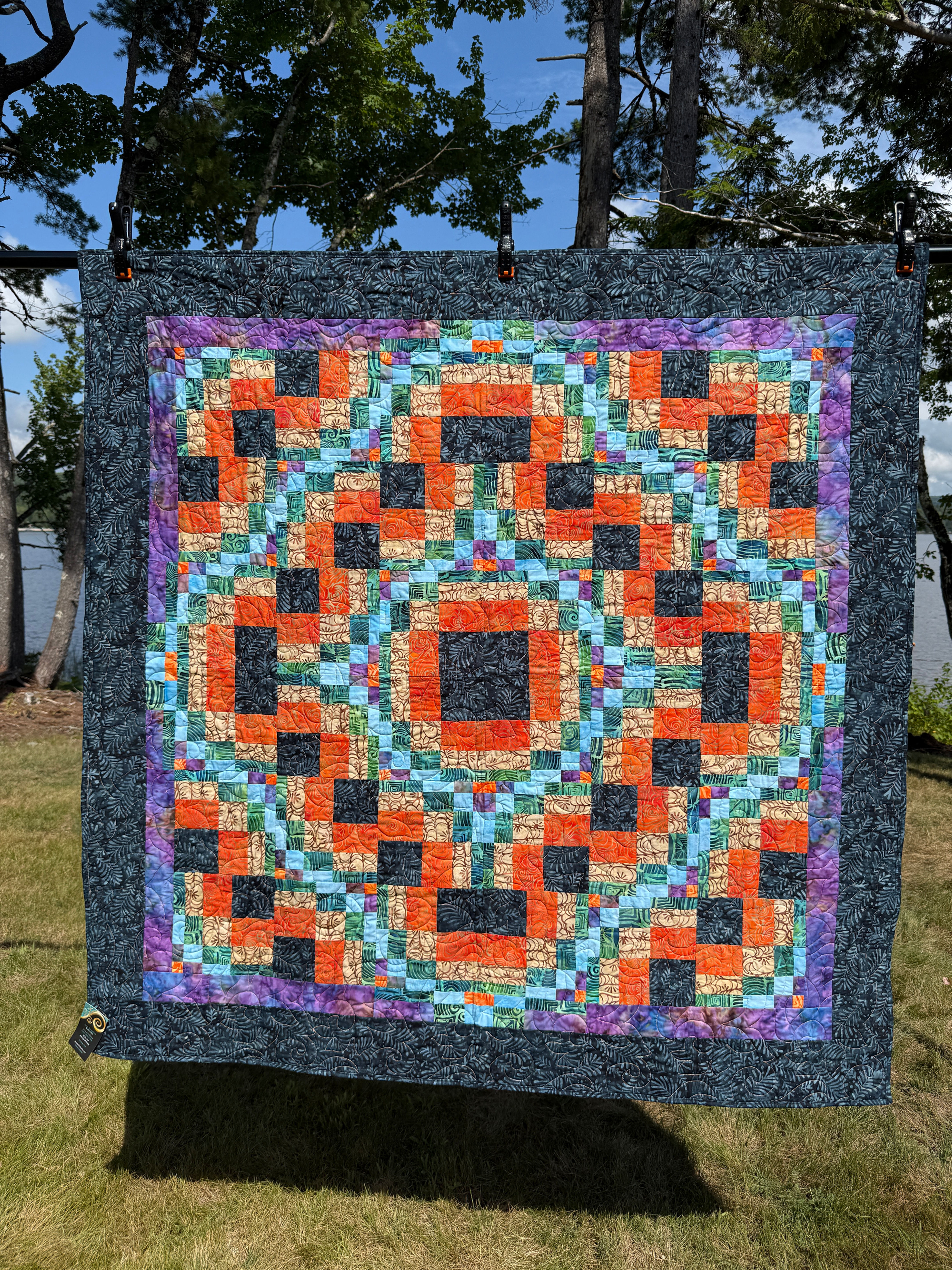 Throw quilt with bargello-style interlocking blocks in orange, black, tan, aqua, and green batiks