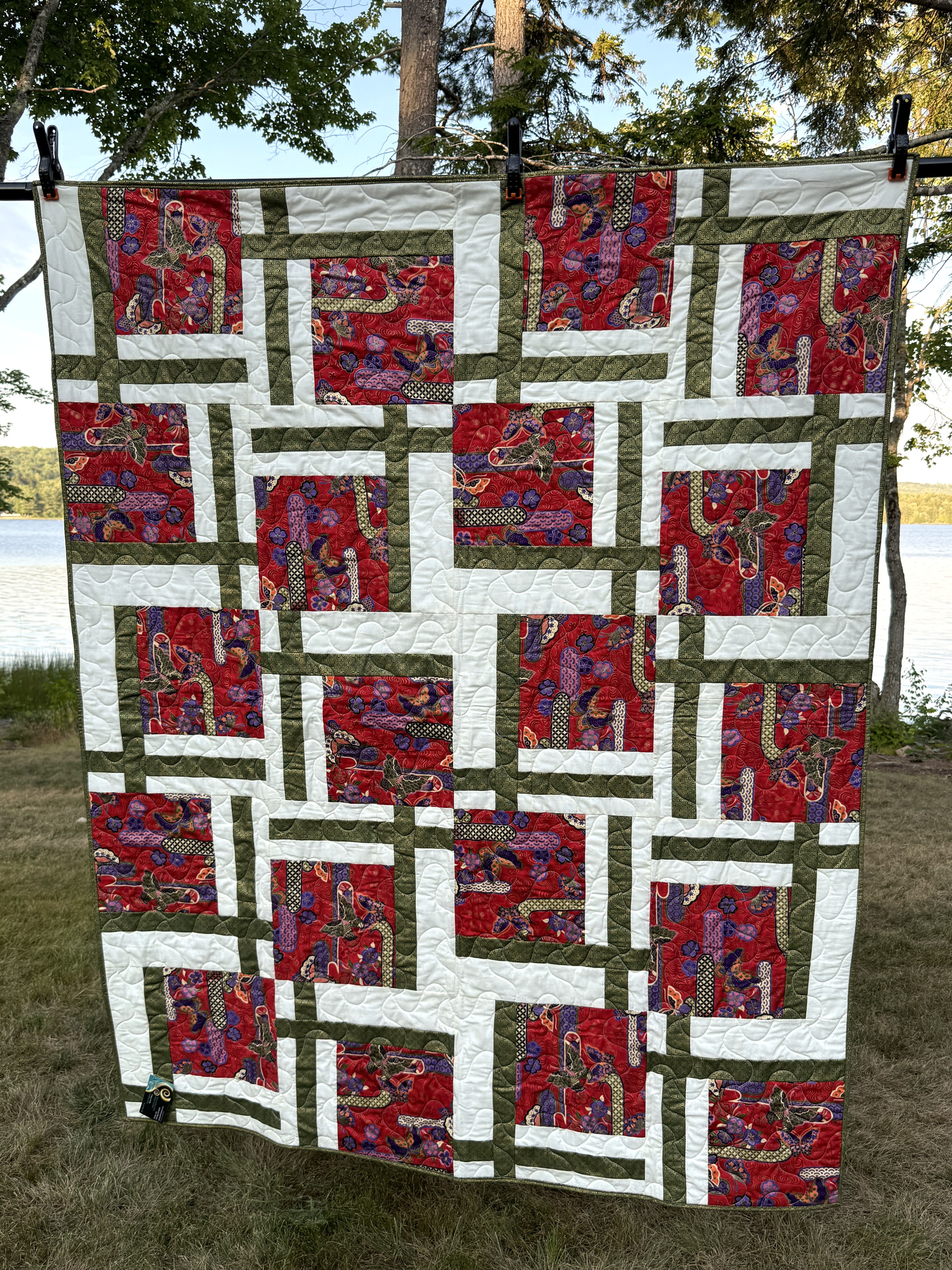 Throw quilt with Asian-themed red butterfly and floral print blocks framed by white and olive green strips