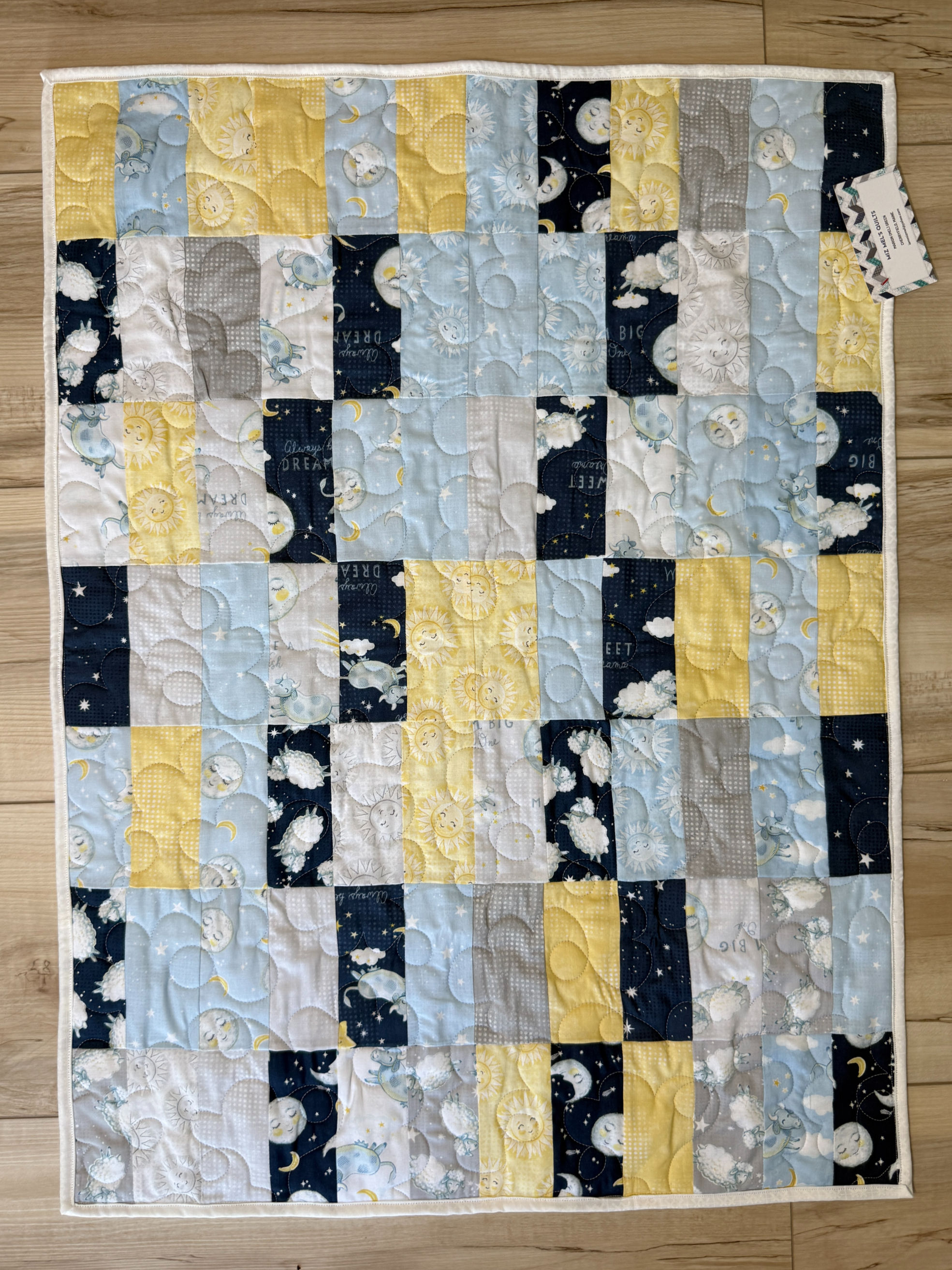 Handmade baby quilt in navy, light blue, yellow, and gray patchwork featuring sheep, cows, moons, suns, and stars
