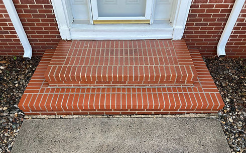 A front porch with recently replaced bricks, where the new bricks and mortar match the original perfectly. The repair is seamless, blending with the surrounding area to restore the porch’s original appearance.