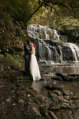 Bride and groom kiss in front of the purakaunui falls in the Catlins