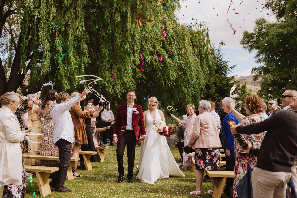 Bride and groom walking down aisle with confetti being thrown and ribbons waved