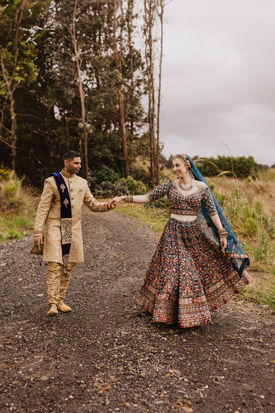 Bride and groom in Indian wedding attire walk hand in hand down the road