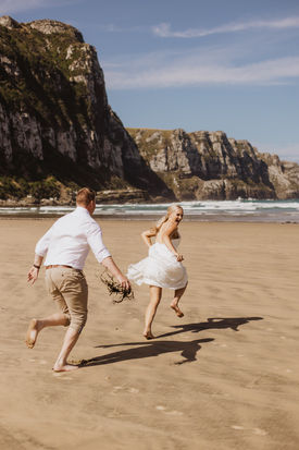Bride and groom running on the beach at Purakaunui Bay in the Catlins