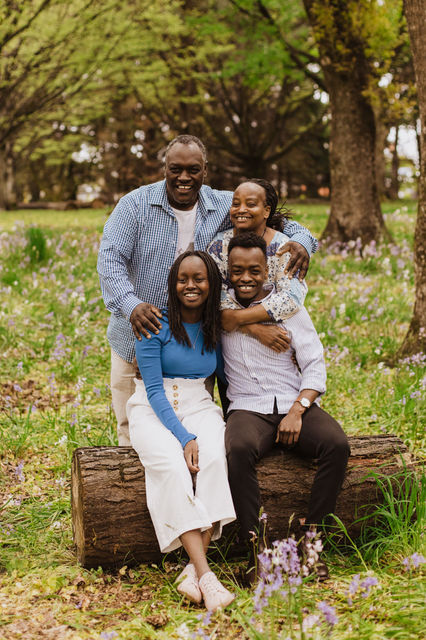 family sitting on a log in the spring flowers in queens park