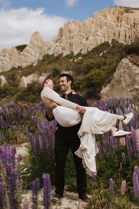 Groom carried bride in the lupins at the Clay Cliffs in NZ