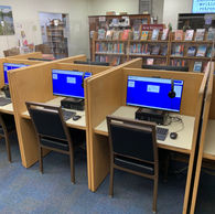 Bank of computers in carrels with chairs and stacks in the background.