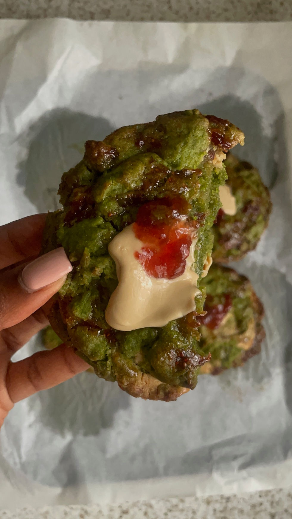 Bakery style matcha cookie marbled with strawberry jam and studded with blonde chocolate, finished with crisp edges and chewy centres and a chocolate and jam piece on top broken in half