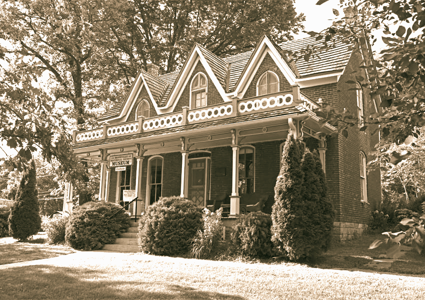 Sepia-toned exterior of the historic Captain Bailey House museum, a Carpenter Gothic home with twin gables and wraparound porch in Brownville, Nebraska
