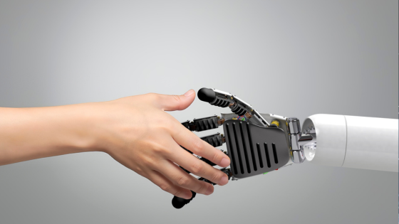 Human and robot hands reaching to shake against a gray background, symbolizing connection between technology and humanity.