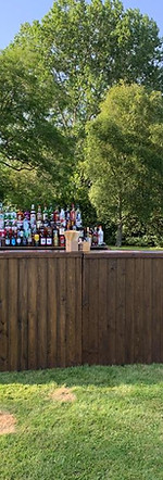 A rustic wooden bar set in an open-air event surrounded by a lush green garden, blending natural charm