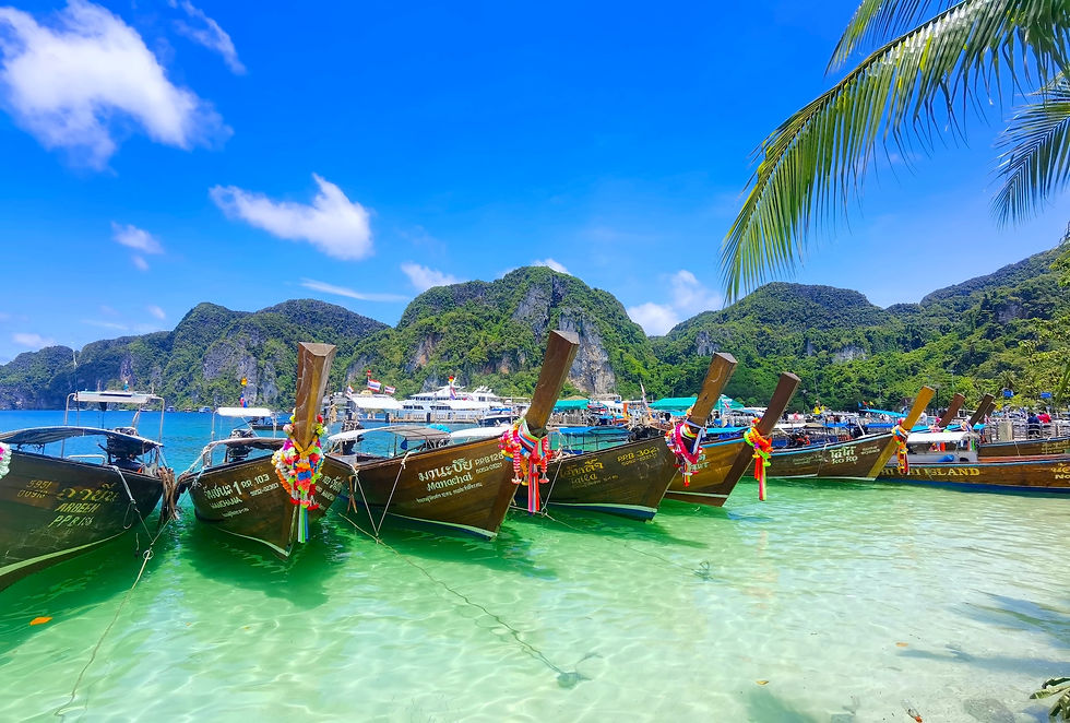 Long-tail boats with Thai text in clear turquoise water, tropical bay and green mountains under a bright blue sky at Phi Phi Don Island.