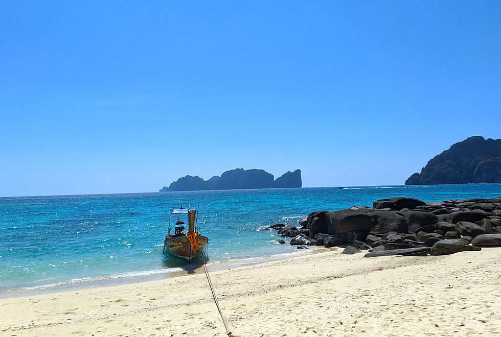 Small decorated longtail boat tied to a sandy beach, with blue sea, rocky shore, and distant islands under a clear sky at Long Beach.