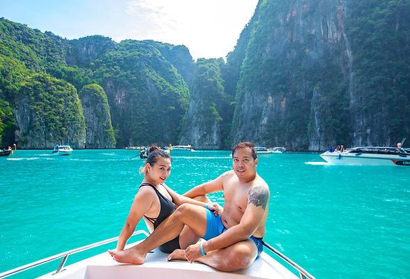 A couple sitting at the front of a speedboat at Pileh Lagoon with limestone cliffs in the background at Koh Phi Phi.