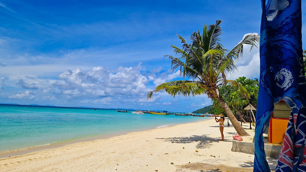 Sunny tropical beach with turquoise water, palm trees, boats offshore, and a woman in a bikini taking a photo at Laemtong Beach.
