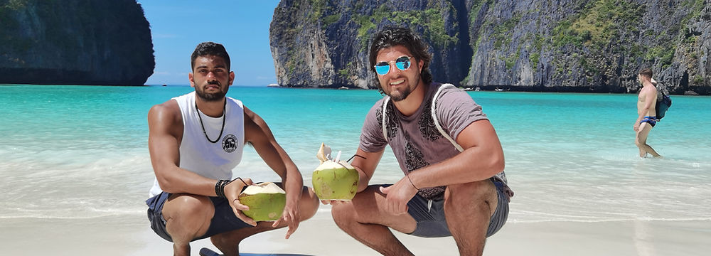 Two men posing at Maya Bay beach in Koh Phi Phi with turquoise sea water.