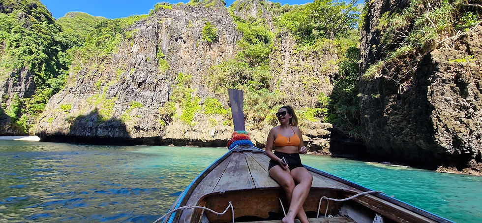 Woman in orange bikini and sunglasses sits on a wooden boat in a turquoise lagoon, smiling at steep green cliffs at Wang Long Bay.
