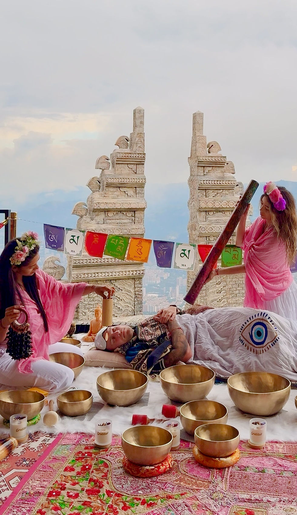 Sesión de sound healing en la montaña, personas rodeadas de cuencos y textiles coloridos, formato vertical, colores cÔlidos y espirituales.
