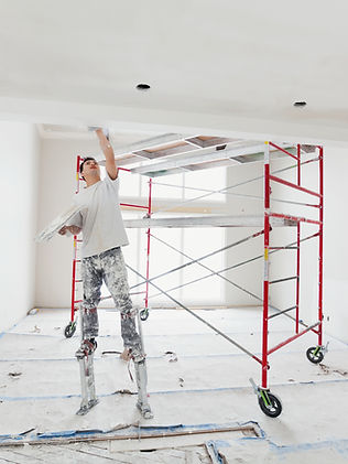 Construction worker working on a drywall with scufolding in the back