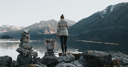 Photo of Kimberley Kufaas facing away from the camera in a cowichan sweater with mountains and an ocean fjord, inlet