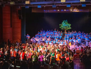 Crianças e educadores no palco se apresentando em um grande coral