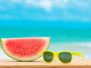 Melancia e óculos escuros em primeiro plano sobre uma mesa e o mar ao fundo