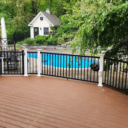Finished composite deck with black aluminum railing overlooking a backyard pool, built by B.E.L. Quality Construction.