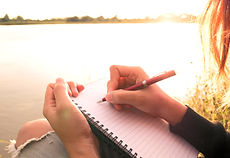 Persona escribiendo junto al agua durante un momento de calma y reflexión