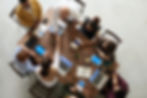 Eight people sitting around a wooden table with devices. Two people are shaking hands.