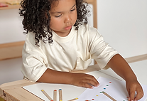 3 year old child doing a matching activity using coloured stickers and lollipop sticks
