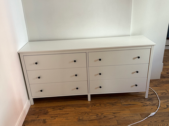 a white dresser with black handles sits on a wooden floor