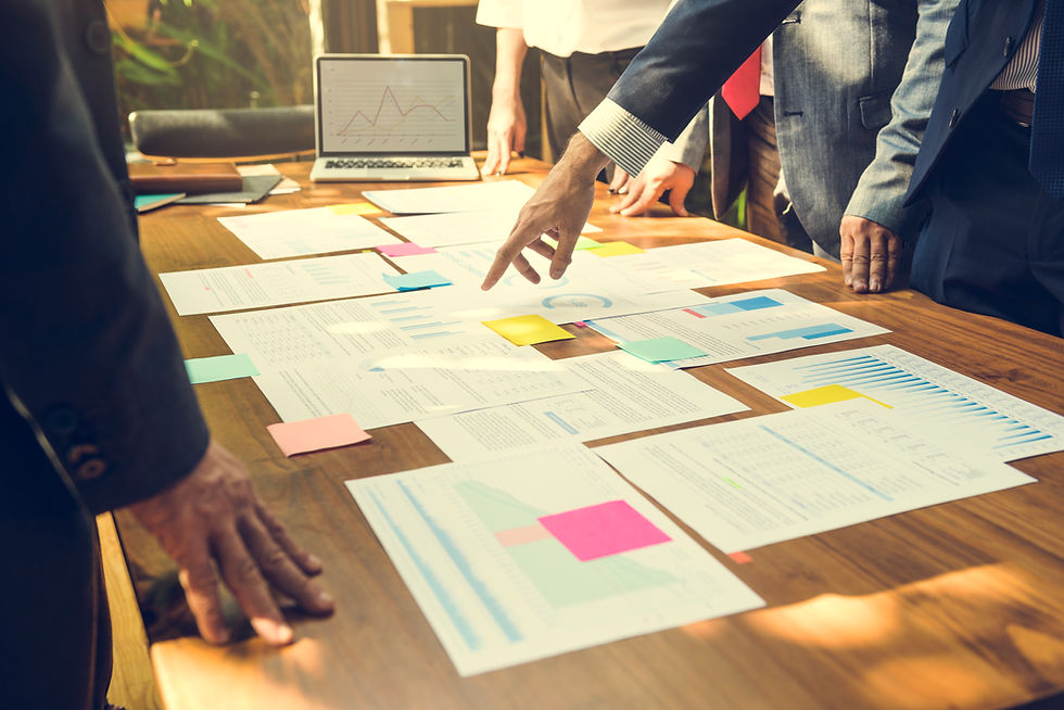 photo of executives meeting at a conference room table reviewing a series of documents with post-it notes displayed across the table with a laptop in the background.standing around the table