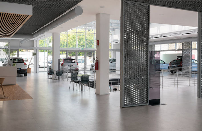 Interno dello showroom Volvo con pilastri, vetrate, pannelli metallici e automobili esposte.