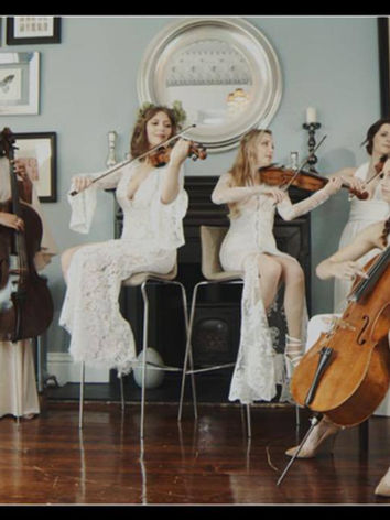 All-female UTC Strings classical ensemble in white performing indoors at an elegant luxury event.