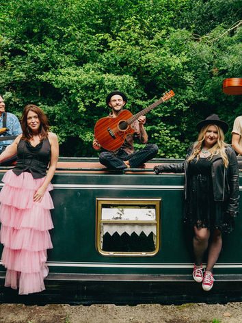 The String Beans posing beside green canal boat in relaxed promo image.