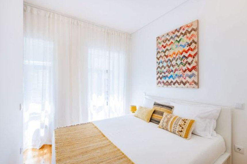 Bright white bedroom, large windows, colorful abstract art, mustard throw.