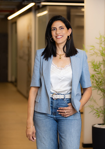 אישה מחייכת בז'קט תכלת וג'ינס במשרד