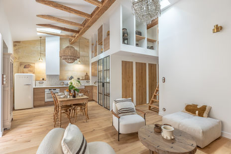 Salon et cuisine d’un appartement rénové à Bordeaux, avec poutres apparentes, verrière et aménagement sur mesure en bois.