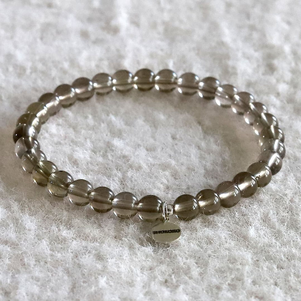 Smoky quartz beaded bracelet with a metallic charm on a soft, white textured surface. The beads are translucent brown