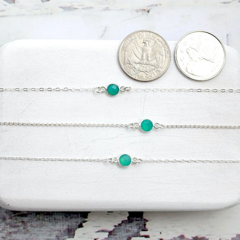 Minimalist sterling silver bezel bracelets with green onyx gemstone, next to two coins. layering sparkling energy for women.