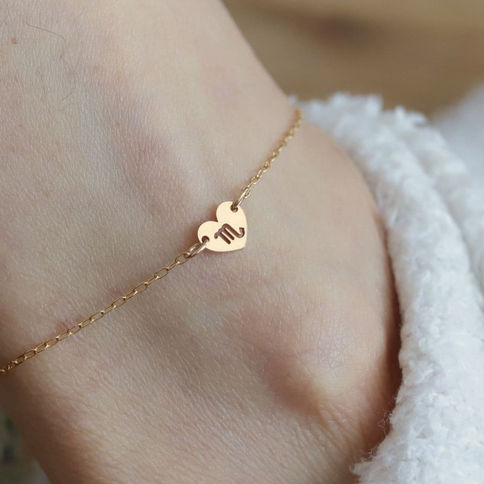 Handcrafted 14k gold filled heart anklet on foot with Scorpio symbol. Wearing cozy white fabric. Calm and delicate mood.