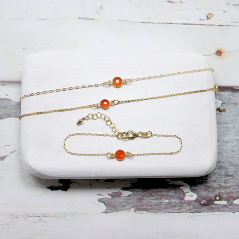 14k gold bracelets with carnelian gems on a white cushion, set against a rustic background. Simple and elegant design