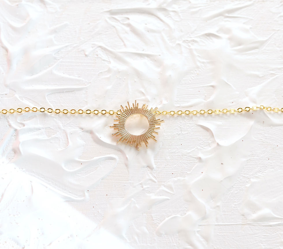 Sunburst gold necklace on a textured white background. The chain features a circular sun motif, creating a bright and elegant