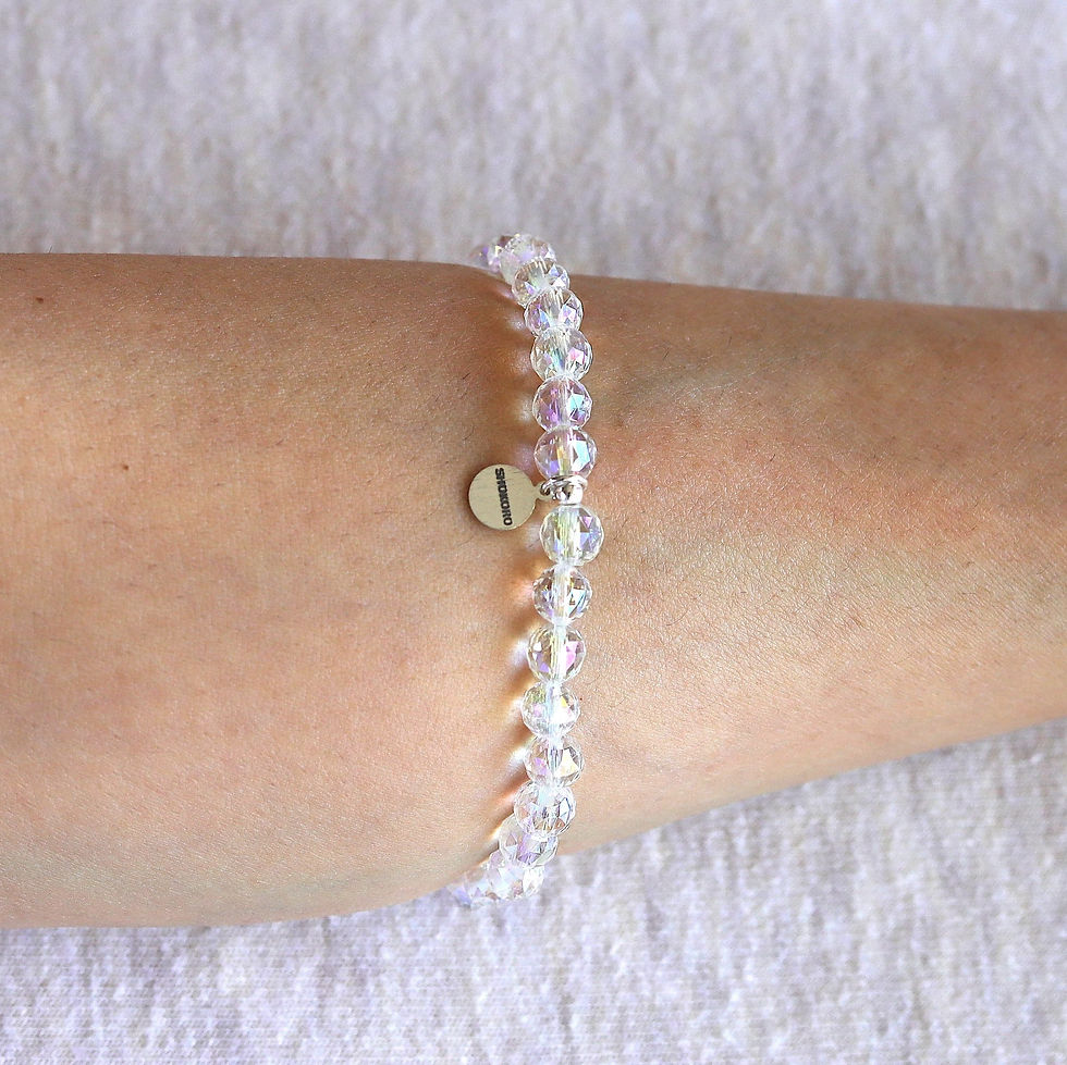 A aura quartz crystal bracelet with a round tag is worn on an arm. The crystals have a subtle rainbow sheen.