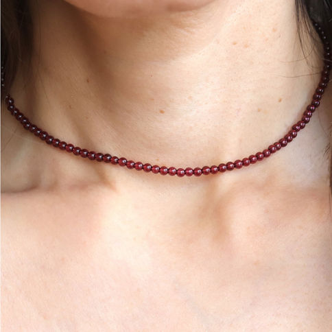 A close-up of a person's neck wearing a string of small, natural red garnet beads as a choker. Skin is smooth.