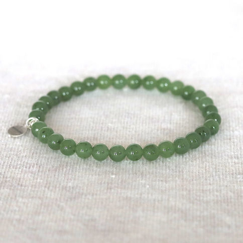 Green jade bead bracelet with a small silver charm resting on a light textured surface. The image has a serene and minimalist