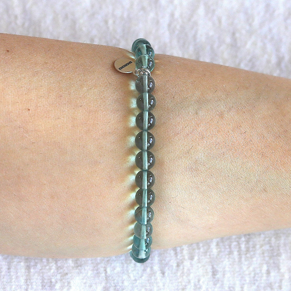 Wrist with a teal blue fluorite beaded bracelet and a small silver tag reading "shokoro". A simple, elegant design.