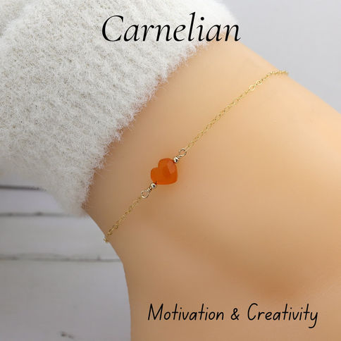 Gold bracelet with an orange carnelian heart charm on a wrist. Text reads "Carnelian" and "Motivation & Creativity."